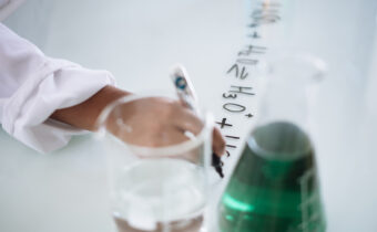 scientist writing mathematical equation on table with beakers